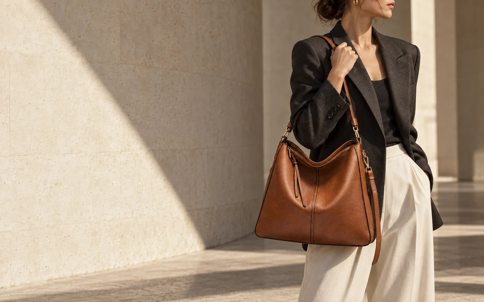 Brown hobo shoulder bag styled with charcoal tailoring in a sunlit stone interior